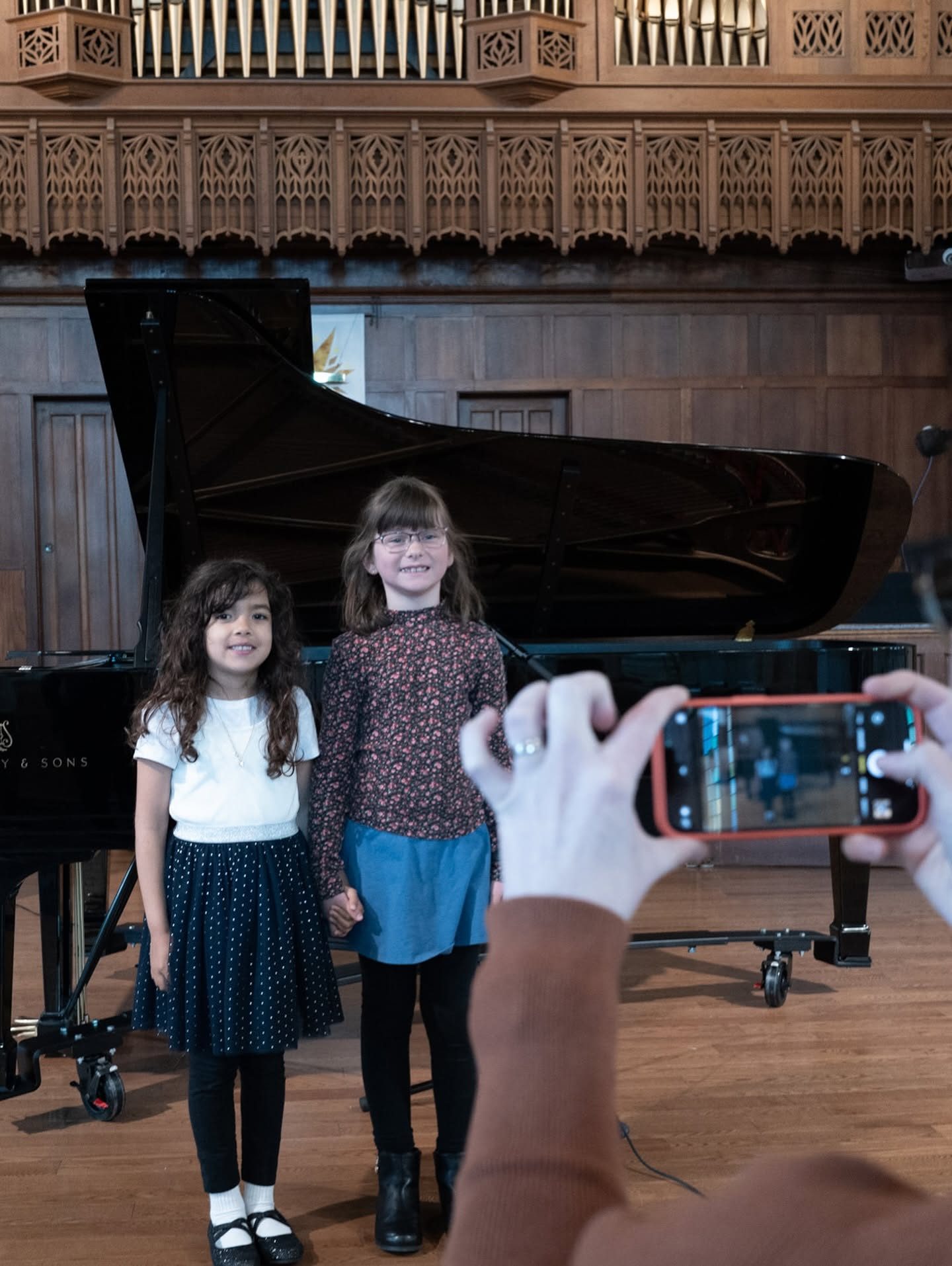 Two young piano students smiling in front of a grand piano at a Piano Place recital